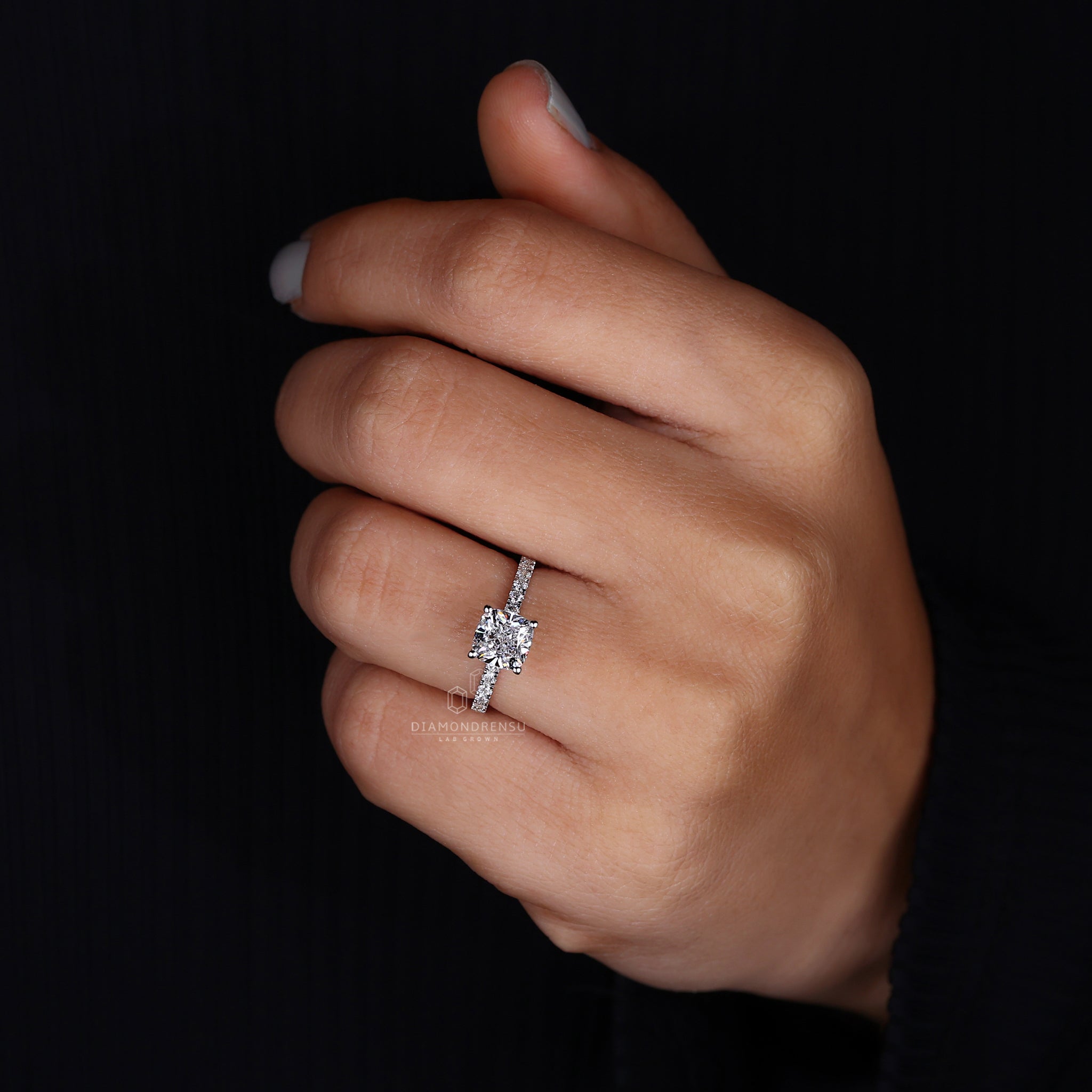 Woman wearing a cushion cut engagement ring with round prong setting.