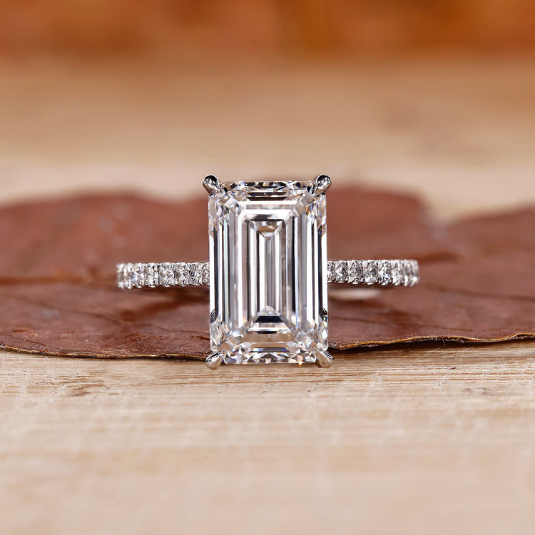 Emerald cut engagement ring with round stone pave accents.
