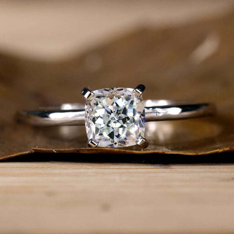 Cushion cut engagement ring with intricate tab prongs.
