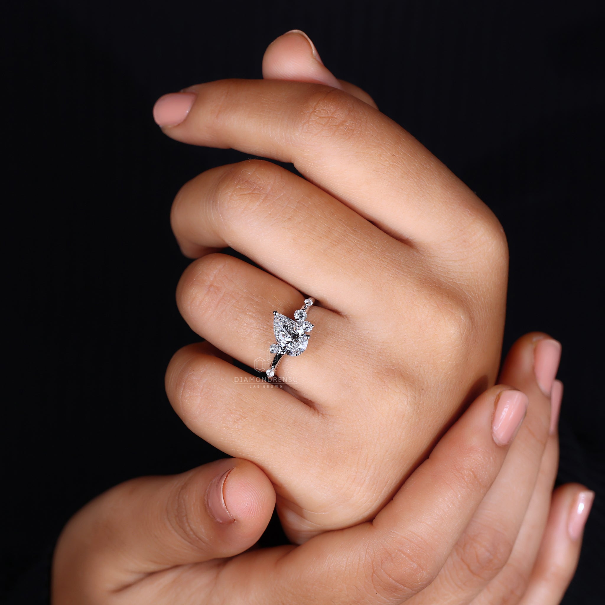 Model's hand adorned with a pear cut diamond engagement ring and round side stones.