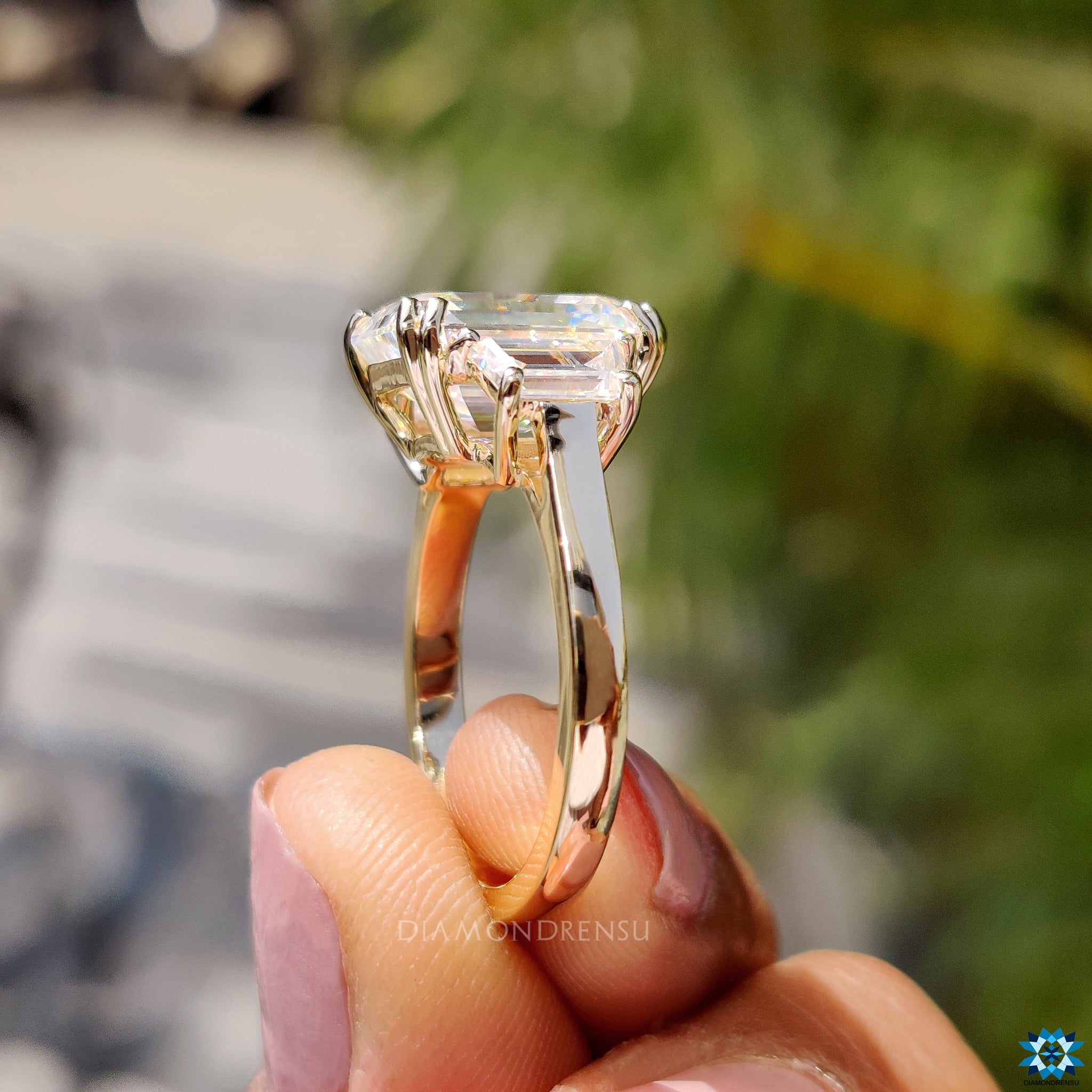 2 trapezoid side stones flank emerald cut moissanite in yellow gold.
