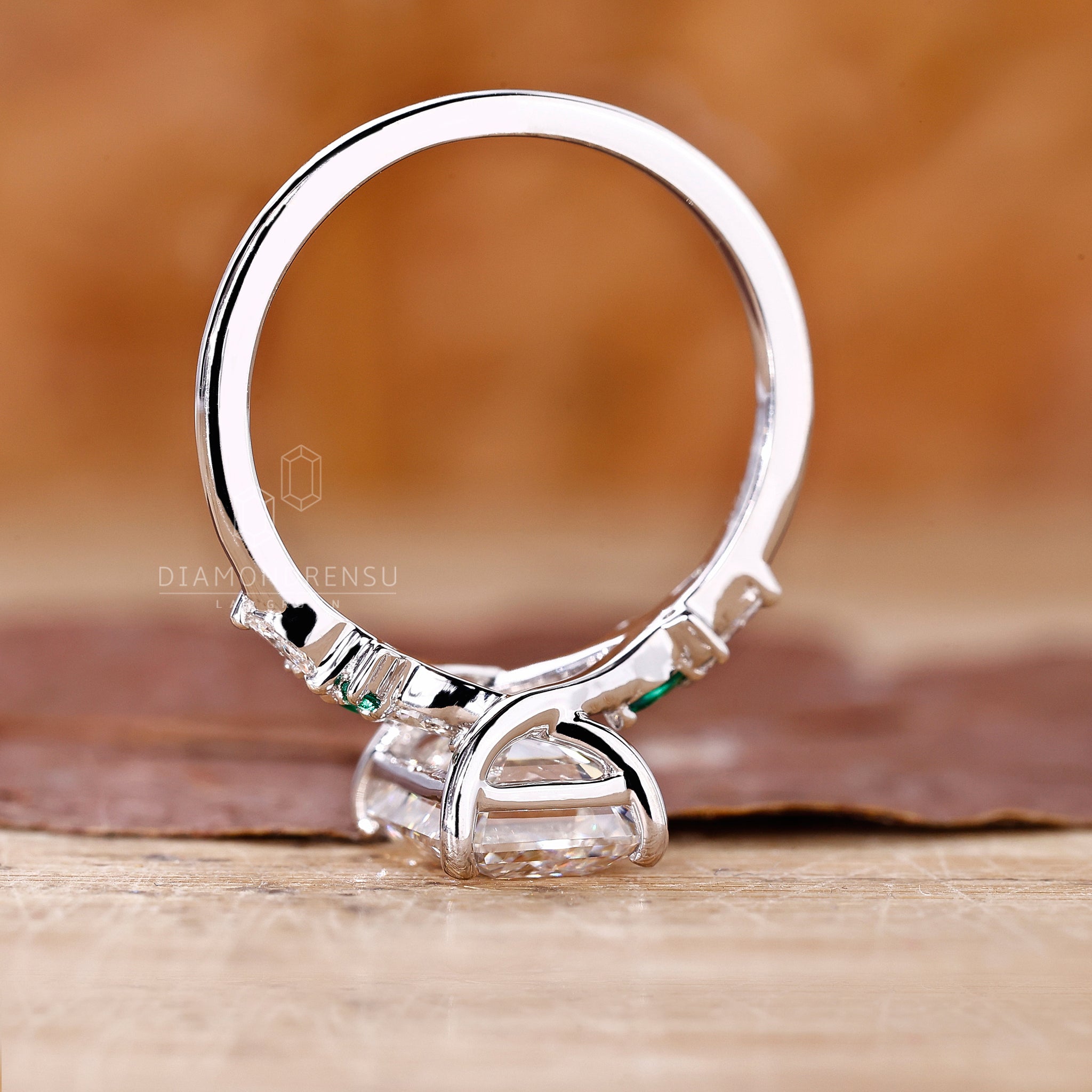 Diamondrensu UK engagement ring with muse setting and green emerald accents.

