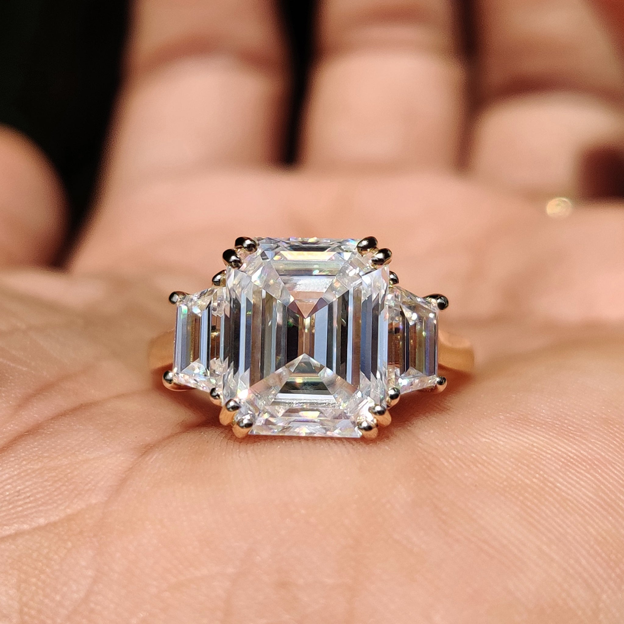 Three stone engagement ring with emerald cut moissanite and trapezoid sides.
