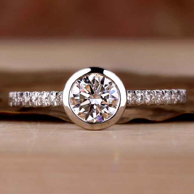 Bezel engagement ring with a round cut diamond and a pave set ring, perfect for timeless elegance.
