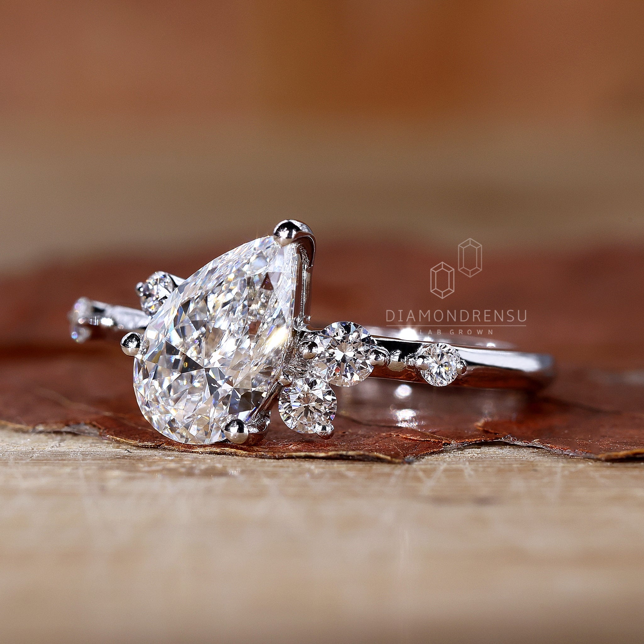 Round side stone engagement ring with a pear cut center diamond.