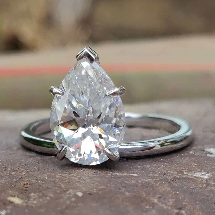 Upside down engagement ring with pear Rensu cut moissanite in a solitaire setting crafted in white gold.
