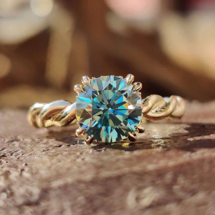 Cyan blue round moissanite solitaire ring in yellow gold.
