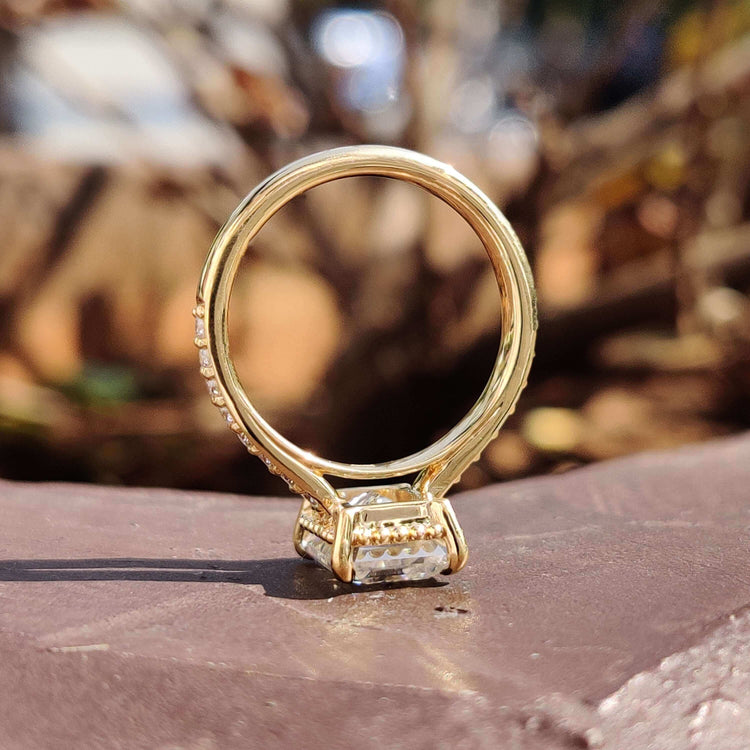 Yellow gold ring featuring an emerald cut moissanite and a round pave band.
