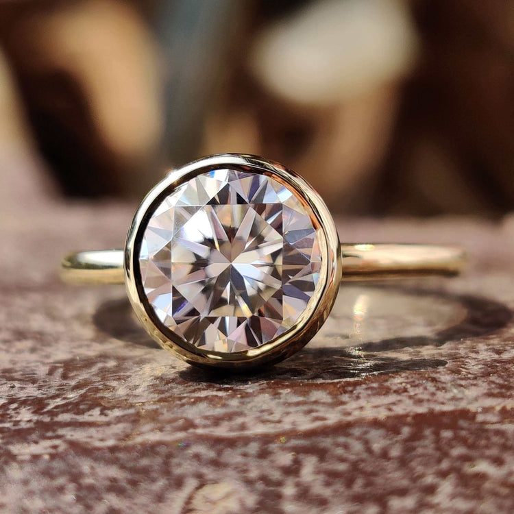Round cut moissanite engagement ring in yellow gold bezel setting.
