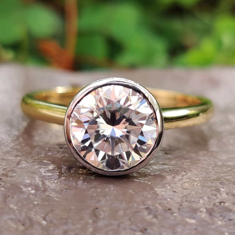 Round bezel set moissanite engagement ring in yellow gold.
