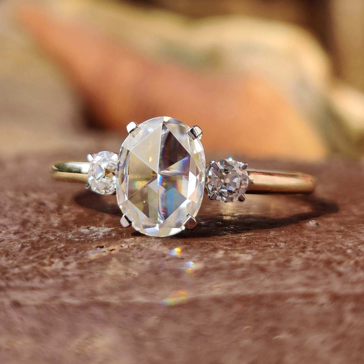Three stone engagement ring with oval rose cut center and round side stones.
