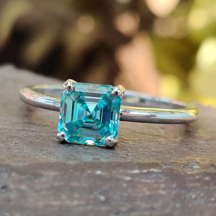 Cyan blue Asscher cut moissanite solitaire ring in white gold.
