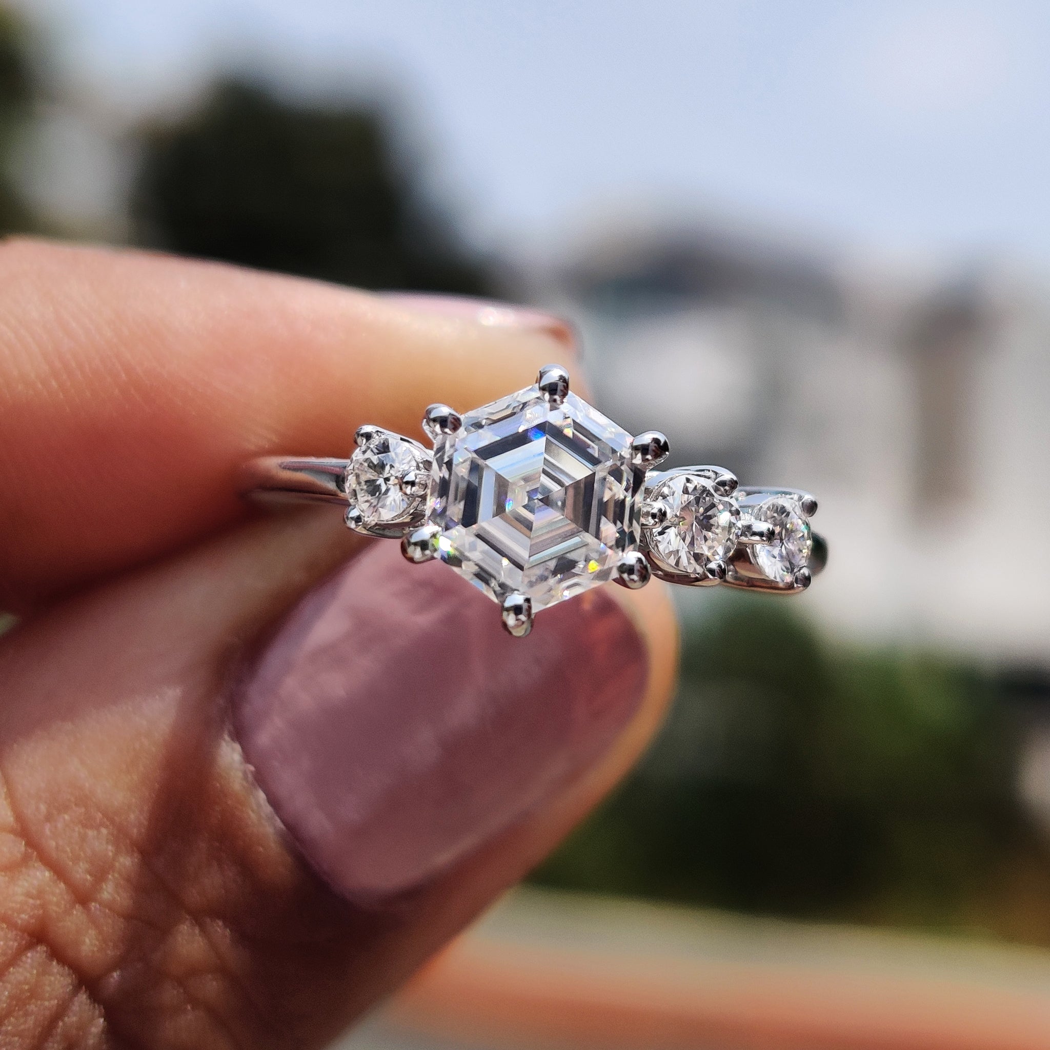 Hexagon engagement ring with round cut side stones in prong setting.
