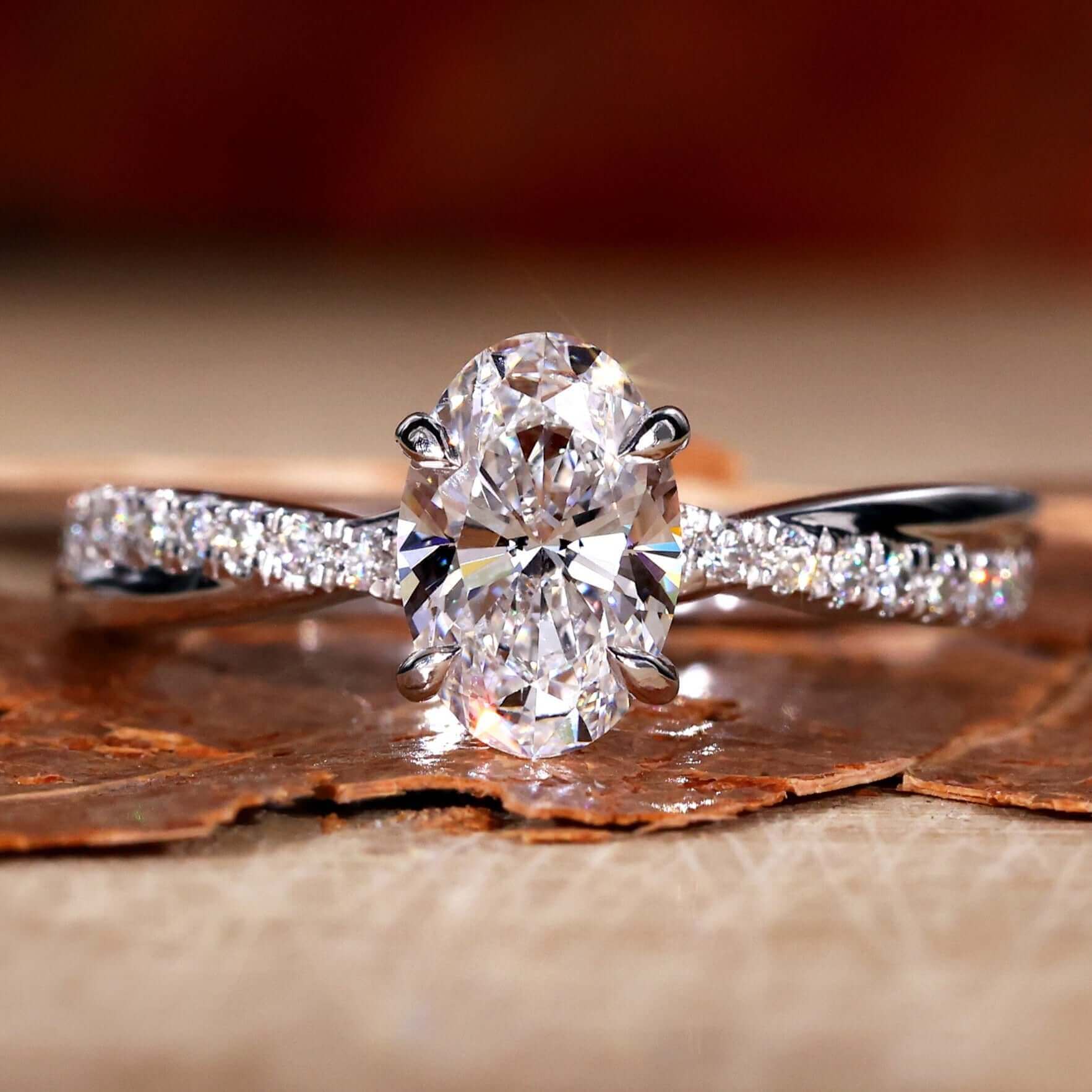 Twisted engagement ring featuring an oval cut Lab Grown Diamond in a 4 prong claw setting with pave accents.
