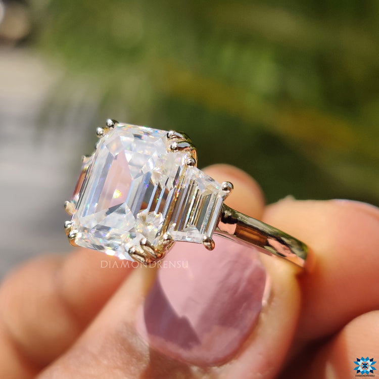 Double prong setting holding emerald cut moissanite and trapezoid side stones.
