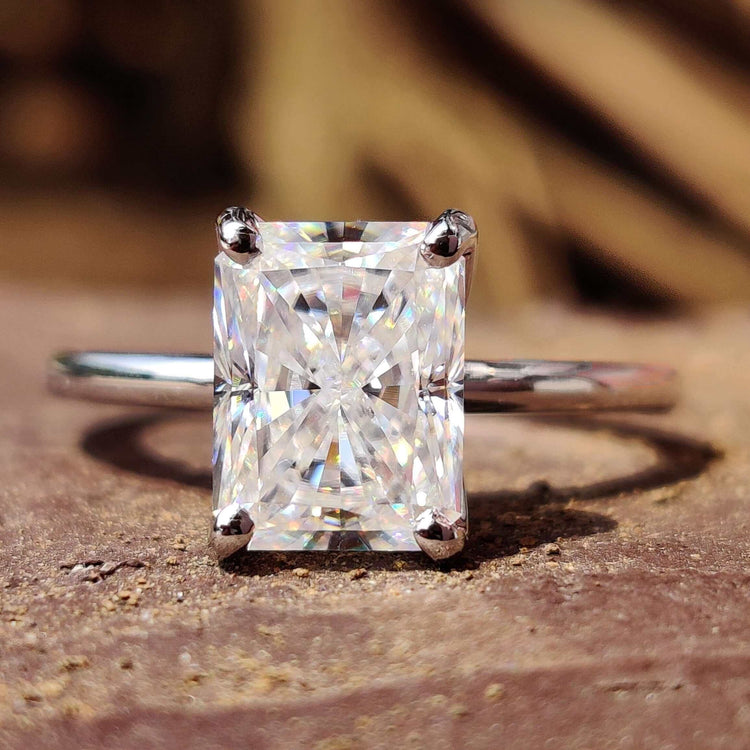 White gold solitaire ring featuring radiant cut moissanite in prong setting.
