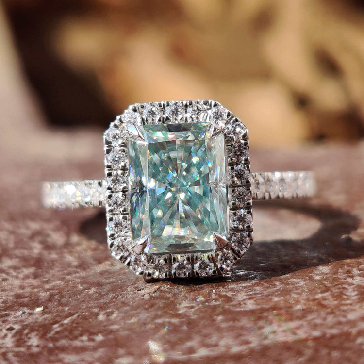 Radiant cut moissanite ring set in white gold with a cyan blue center stone.
