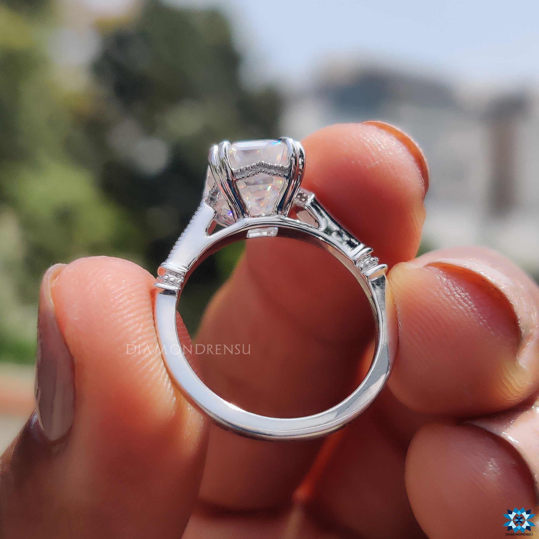 Milgrain ring featuring emerald cut moissanite and round side stone accents.
