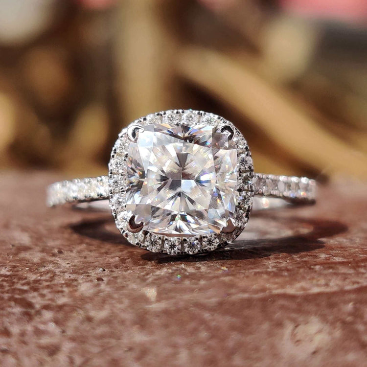 Cushion cut moissanite engagement ring with halo and round side stones.
