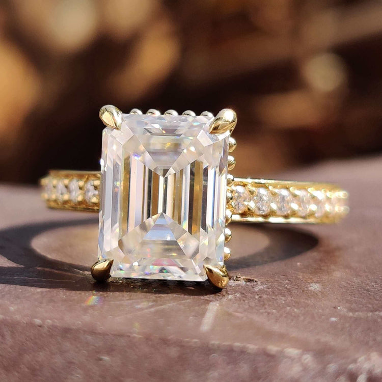 Emerald moissanite engagement ring set in yellow gold with round cut pave accents.
