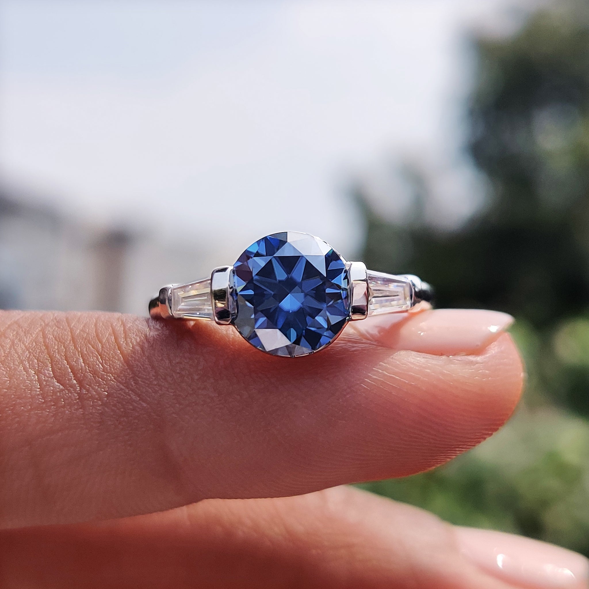 Blue moissanite engagement ring with tapered baguette side stones.
