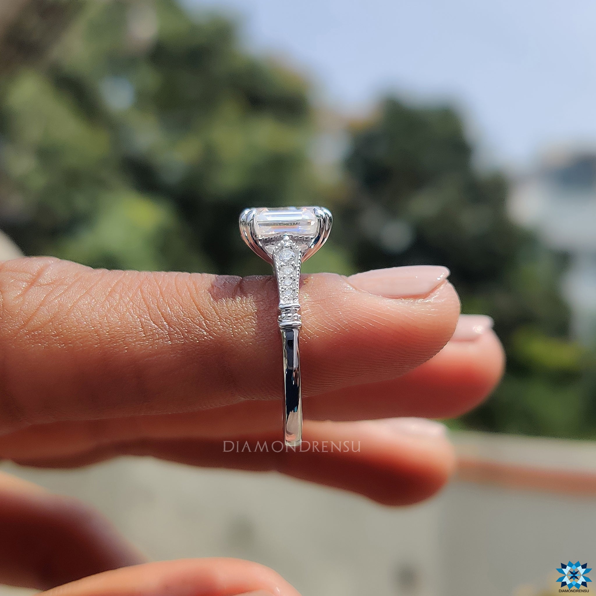 Double claw prong ring with emerald cut moissanite and side stones.
