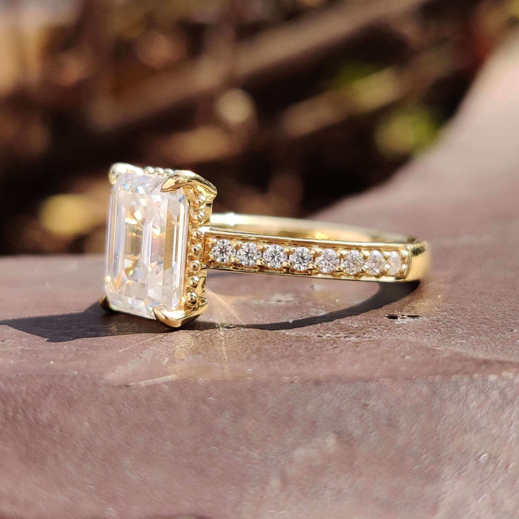 Cathedral style emerald moissanite ring in yellow gold with prong setting.
