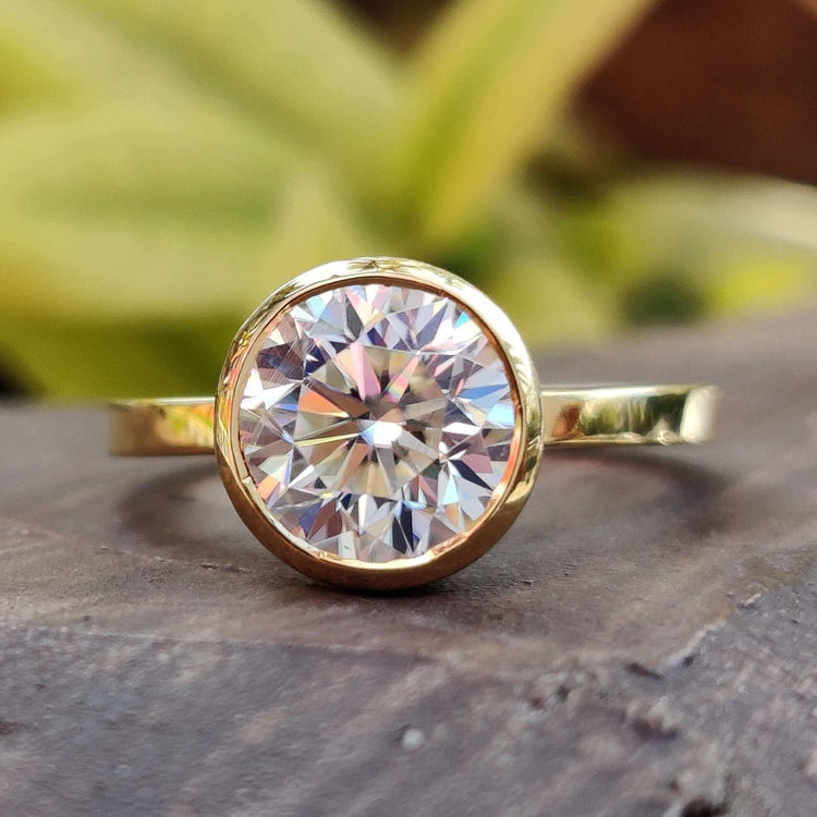 Bezel set Moissanite ring with round cut stone in a custom yellow gold solitaire setting.
