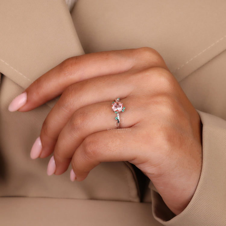 Peach sapphire ring with green emerald accents and prongs.
