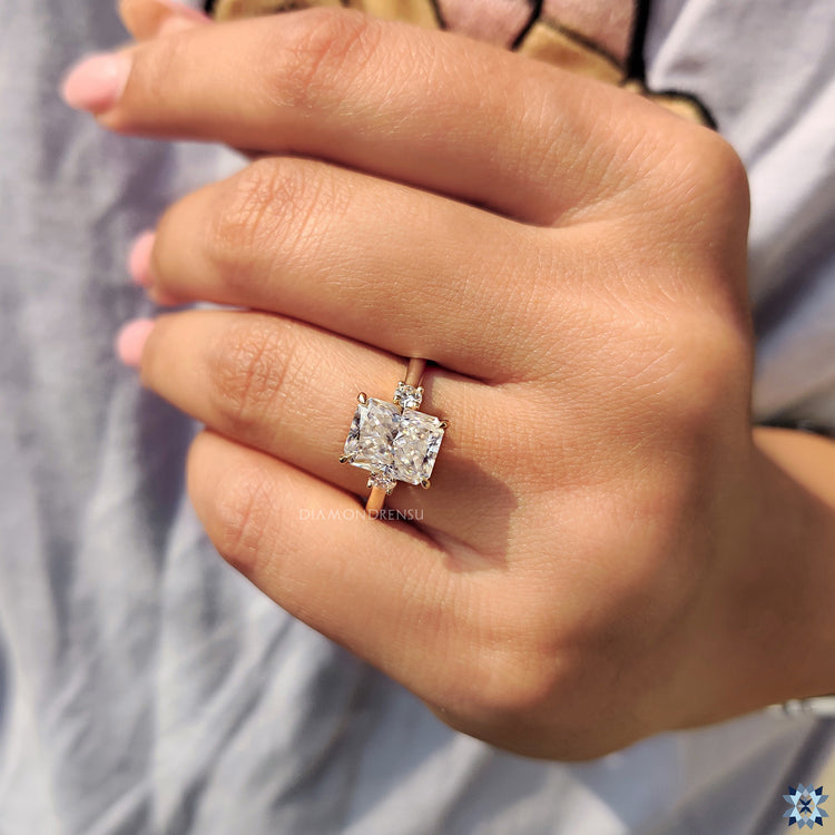Radiant moissanite ring set in yellow gold with round side stones.

