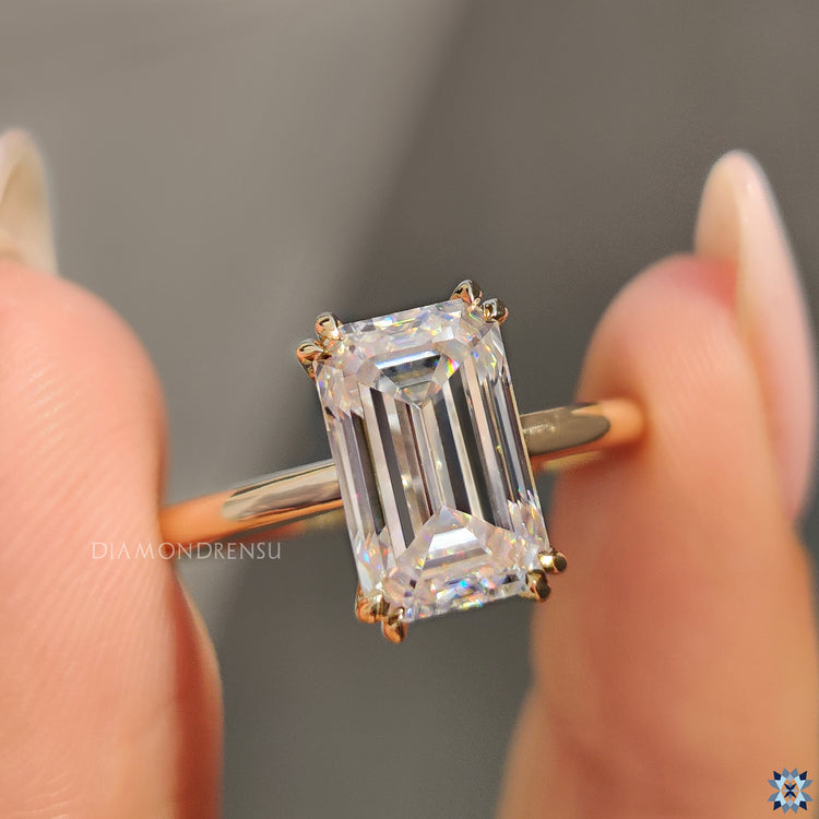 Moissanite engagement ring featuring emerald cut and handmade yellow gold band.
