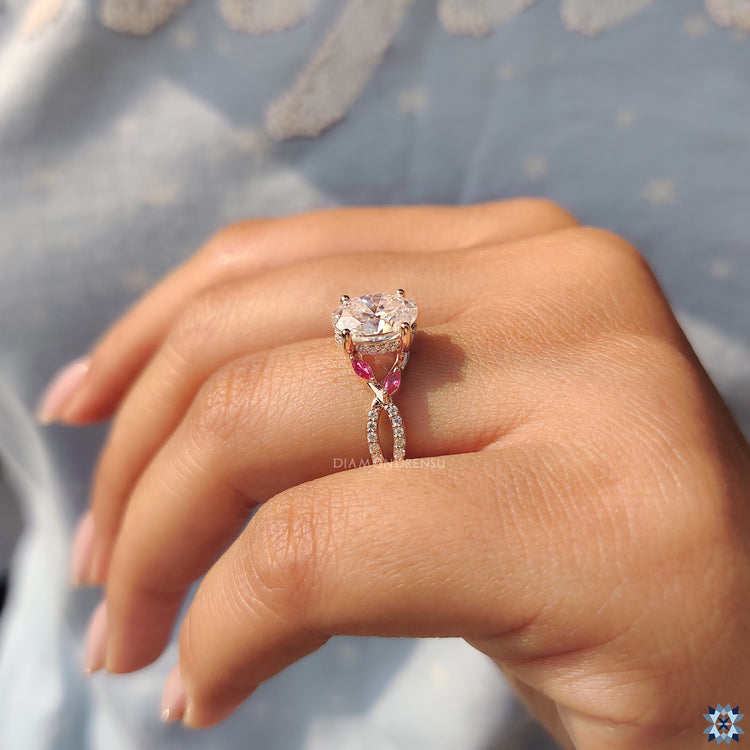 Rose gold moissanite ring with oval stone and red marquise side detail.
