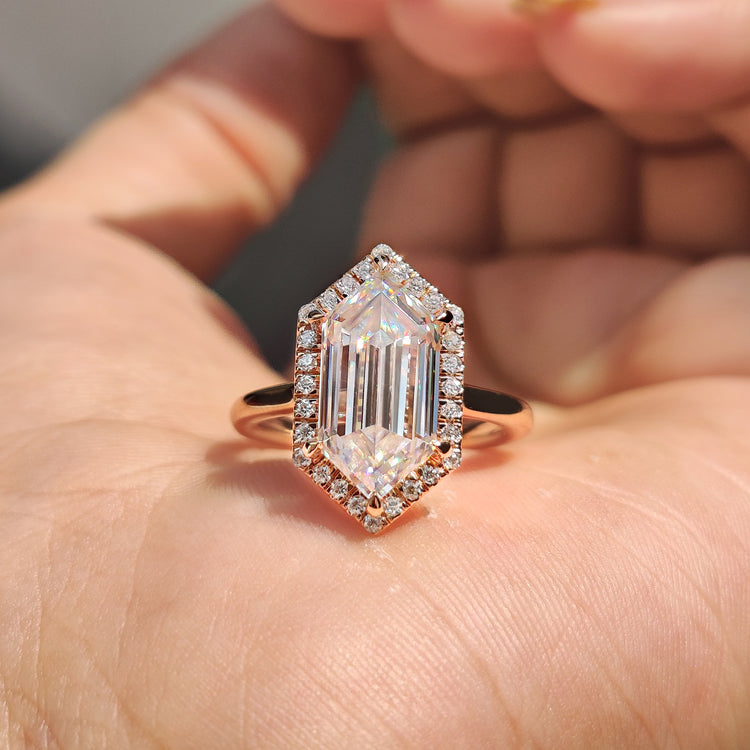 Elongated hexagon engagement ring in rose gold with a halo design.
