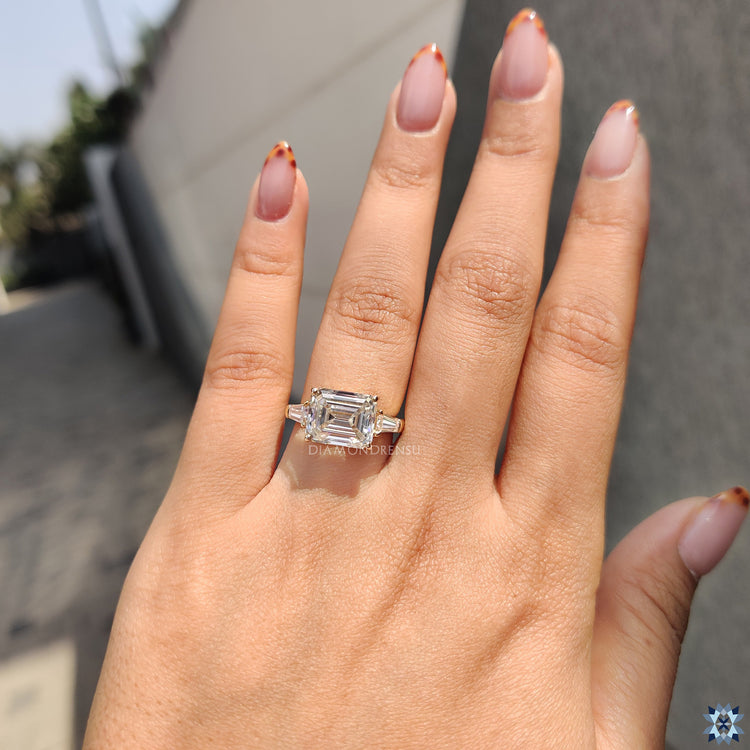 East West engagement ring featuring emerald cut and tapered baguette accents.
