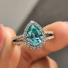 Pear cut engagement ring featuring cyan blue moissanite and round halo.
