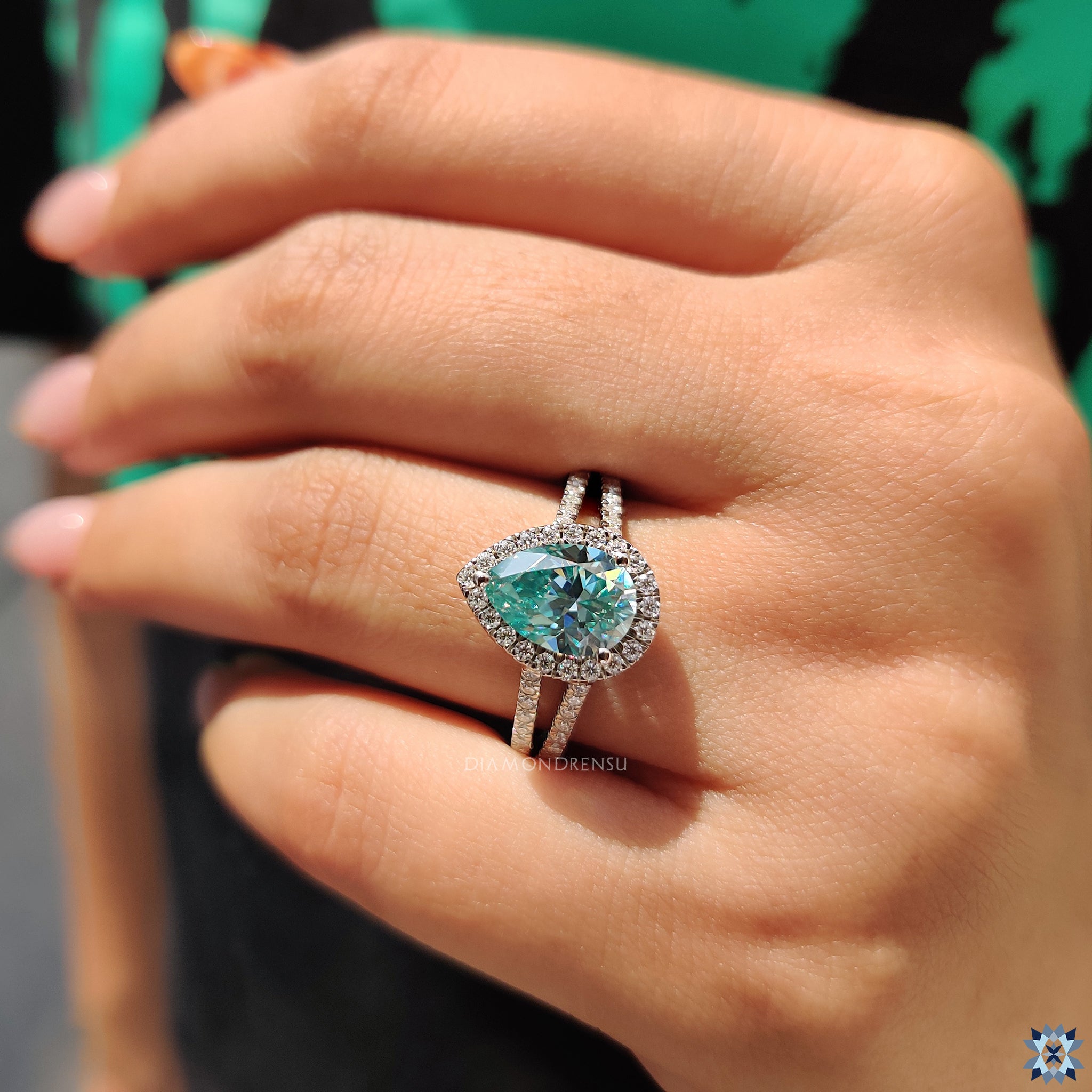 Cyan blue pear cut moissanite in a three-prong round halo setting.
