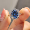 Oval cut dark blue moissanite engagement ring with round cut halo and cathedral setting.

