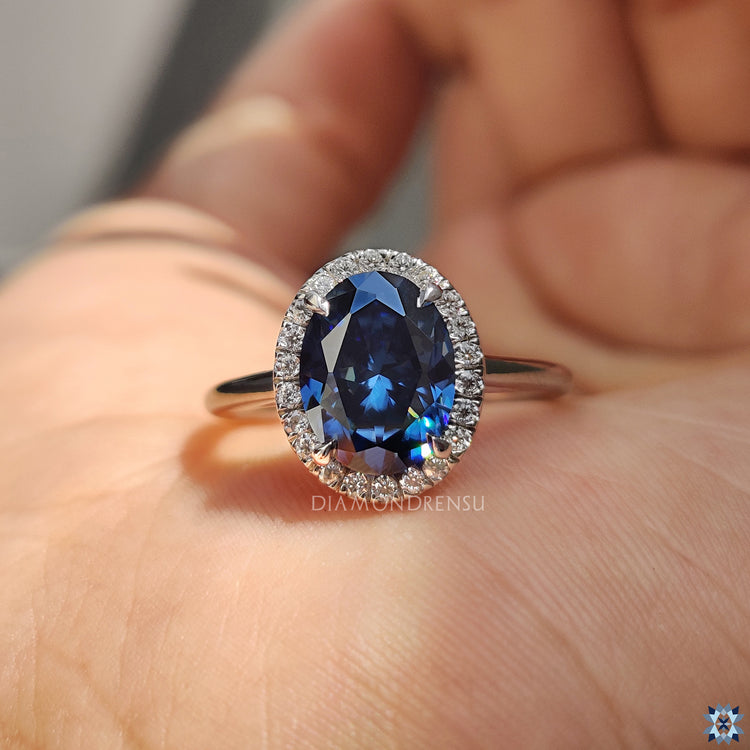 Dark blue oval moissanite engagement ring with round halo and classic 4 claw prongs.
