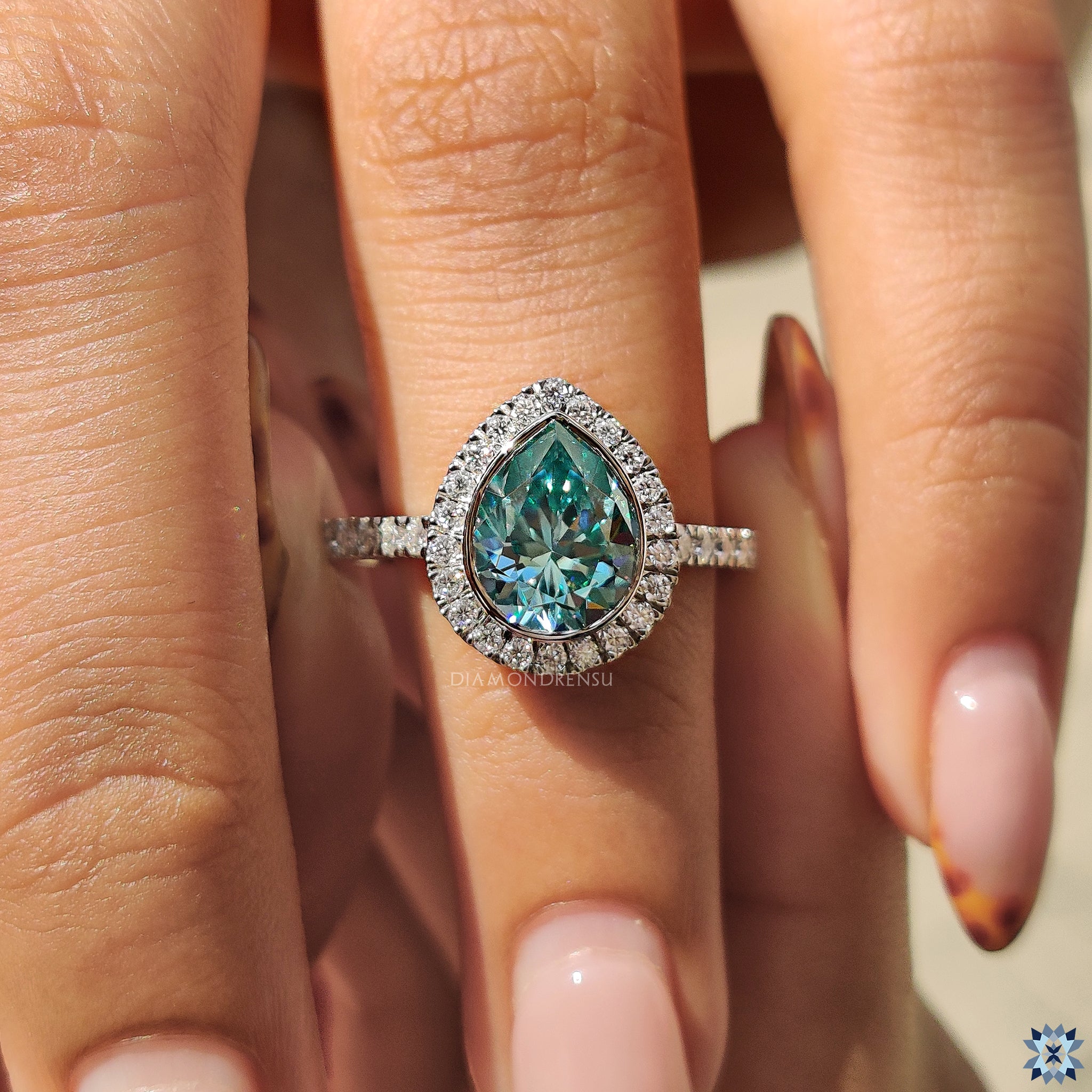 Stunning cyan blue moissanite pear ring with halo and prong design.
