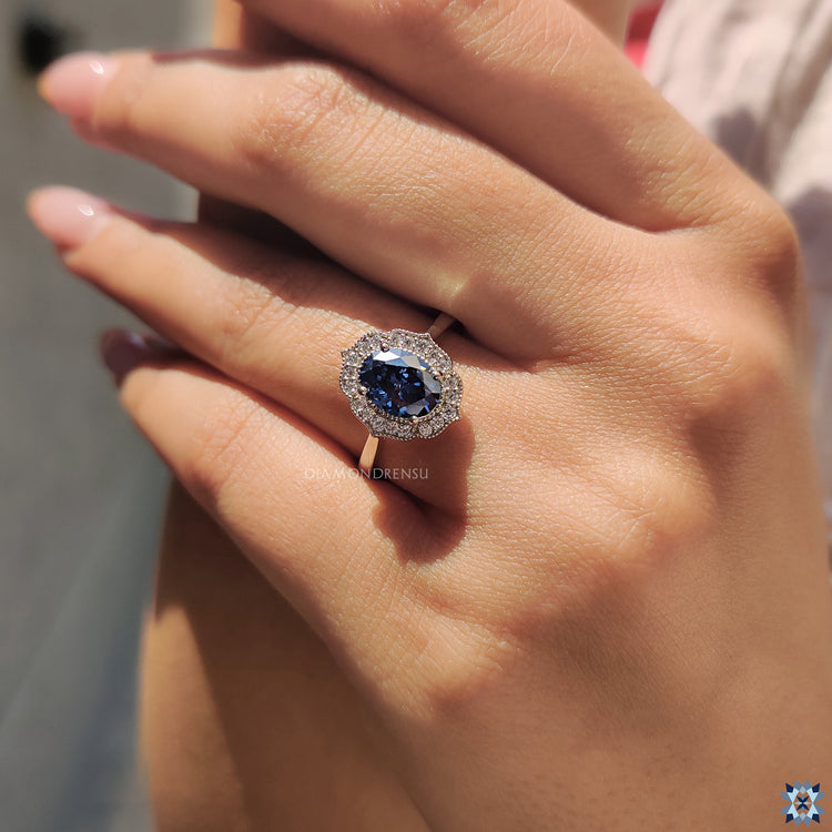 Oval dark blue Moissanite ring with halo and milgrain edge in prong setting.
