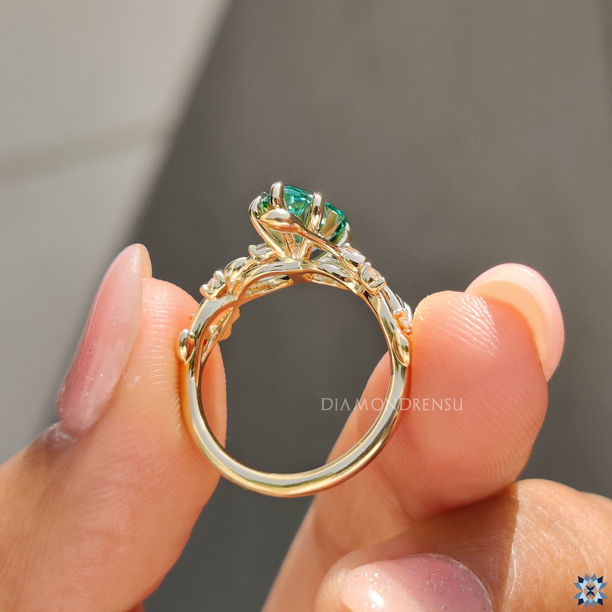 Pear cut moissanite ring with natural leafy design and vibrant green gemstone.
