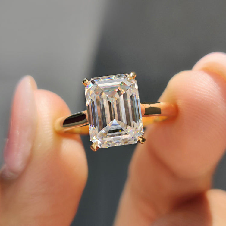 Emerald cut solitaire moissanite ring with 4 prong setting in yellow gold.

