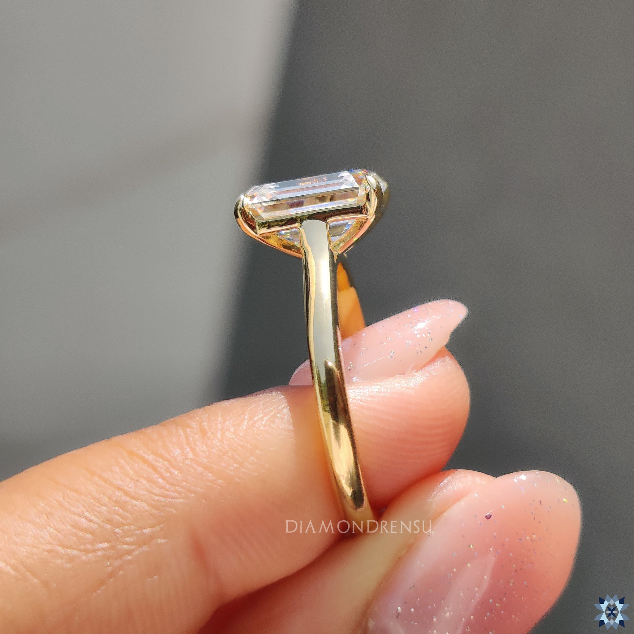 Emerald cut moissanite solitaire ring with timeless four prong mount in yellow gold.
