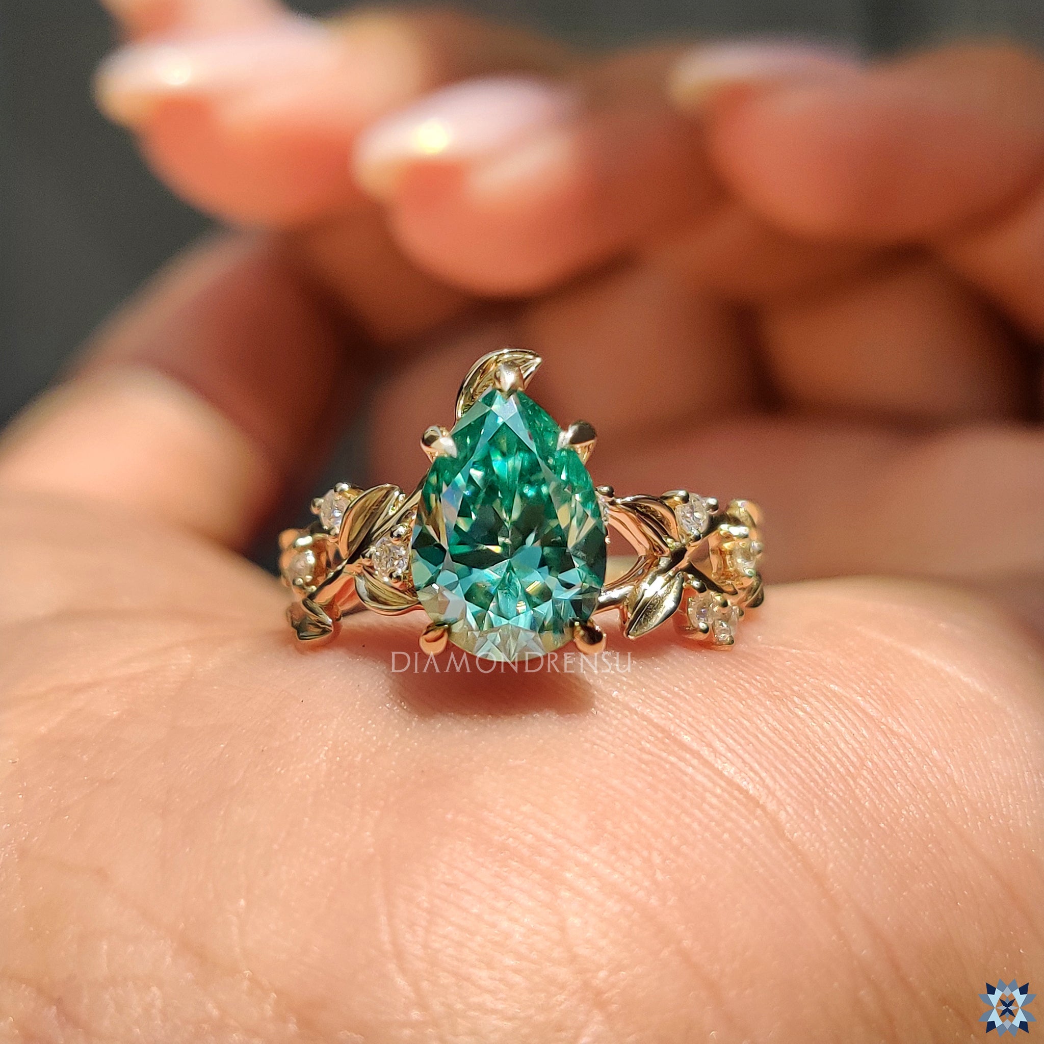 Green moissanite pear cut ring with natural motifs and elegant yellow gold finish.
