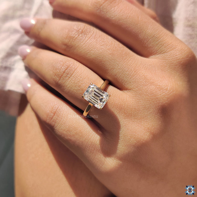Cathedral setting moissanite ring with emerald cut stone and handcrafted yellow gold band.
