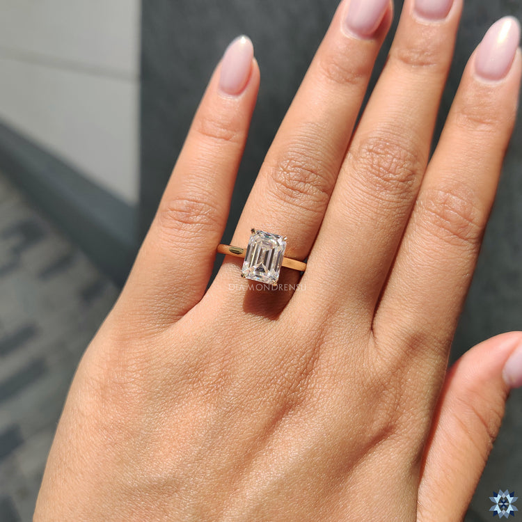 Yellow gold engagement ring with emerald cut moissanite and minimalist solitaire style.
