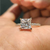 Moissanite gold ring with princess cut stone and round cut pave band in yellow gold.
