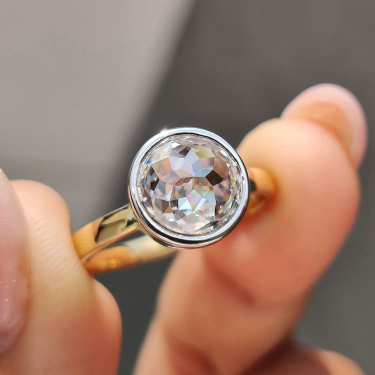 Bezel engagement ring with round rose cut Moissanite in two-tone gold setting.

