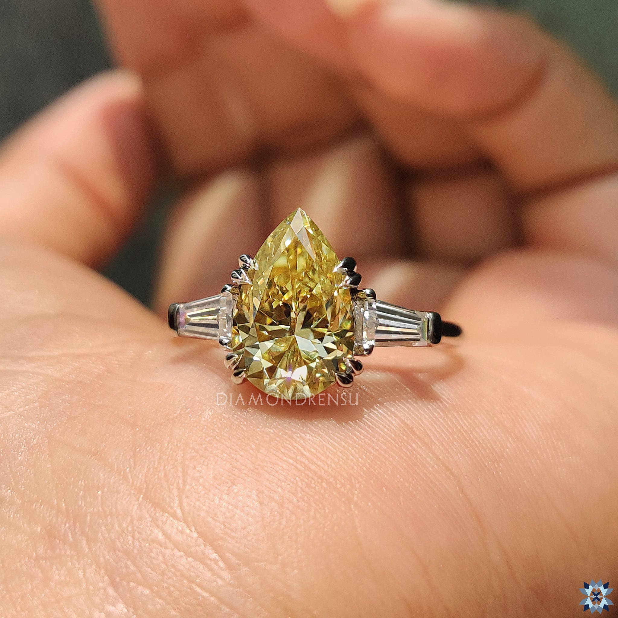 Diamondrensu UK engagement ring with pear three stone design and yellow Moissanite center.
