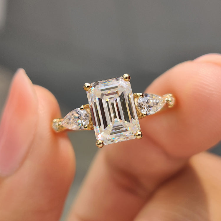 Moissanite emerald cut engagement ring with two pear cut side stones in yellow gold.
